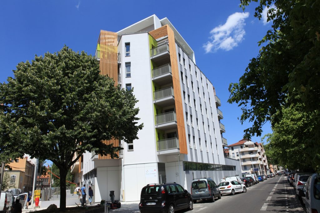 Vue ensoleillée de l'immeuble construit à Lyon, façade blanche et brise-vue en bois